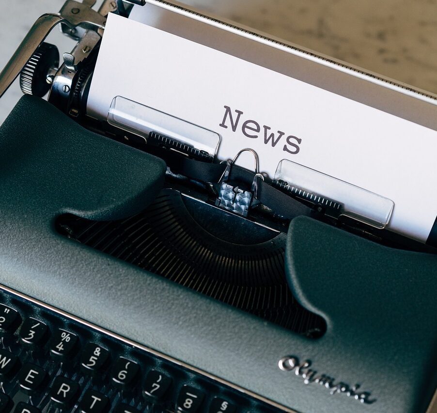 Vihreä kirjoituskone, jossa paperilla sana News.
